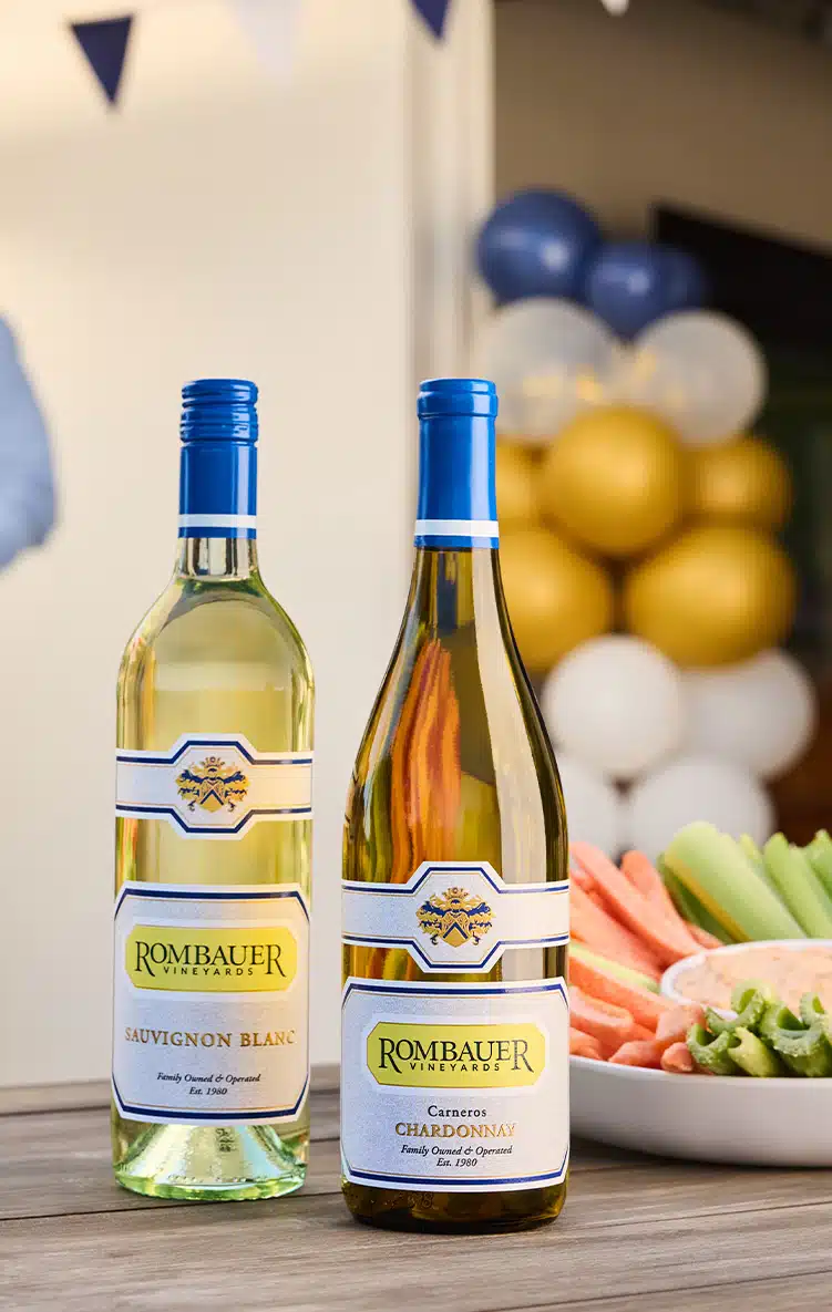 Chardonnay and Sauvignon Blanc on a table at a tailgate next to buffalo chicken dip and veggies.