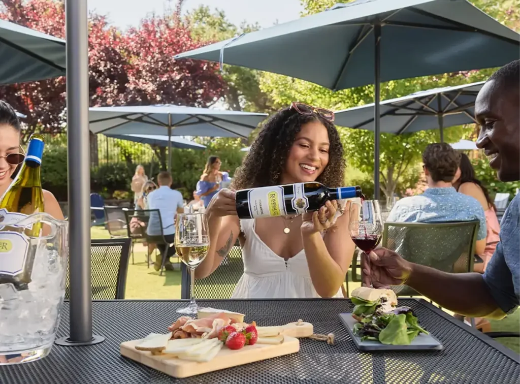 Person pouring wine into a glass at a table outside